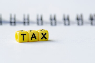 TAX text on colorful plastic alphabet beads with blurred notepad background