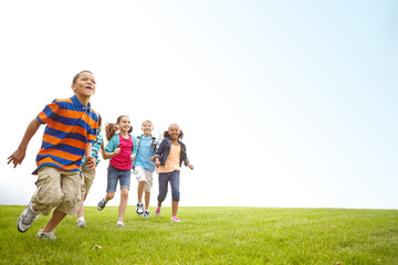 Obraz premium Fun, running and group of kids on grass for outdoor games, race and happy development space. Diversity, energy and children playing in field together with smile, growth and summer mockup on low angle