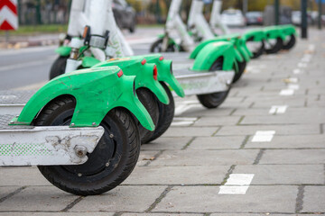 
several electric scooters parked on the sidewalk. Scooters are green in color and have large wheels.