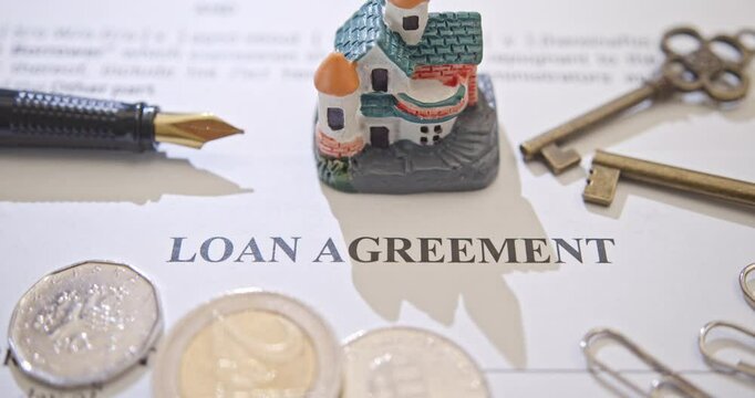 Loans, financial agreements, mortgages, real estate, and home ownership. A loan agreement document with a small model house, a fountain pen, coins, symbolizing the financial agreement and planning.