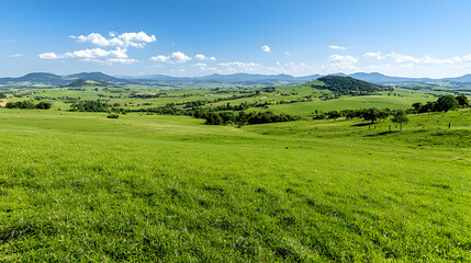 Naklejka premium Sunny day, green rolling hills, distant mountains, clear sky, pastoral landscape, ideal for travel brochures