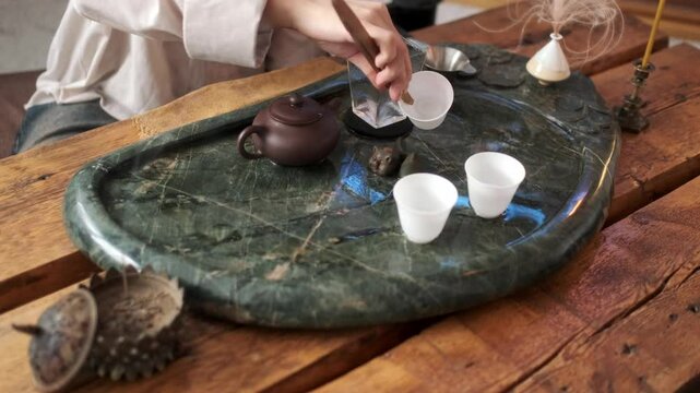 Close-up: a girl in a light shirt prepares for drinking tea, washing the paraphernalia for the tea ceremony with hot water.