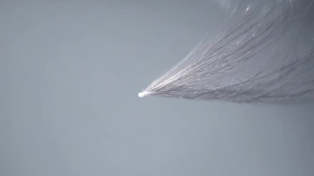 Establishing video, camera slowly zooms in on a single, gently shimmering, silver fiber optic thread against a gray background, muted lighting, subtle, delicate visual, texture