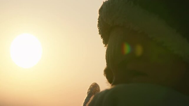 Cold woman with beanie and face covering at sunrise, close up handheld shaky sunflare in 4k
