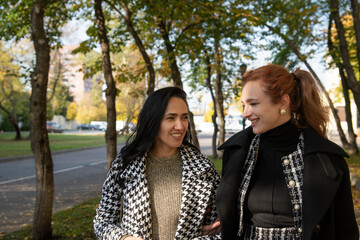 Fototapeta premium Two women enjoy an autumn walk along a tree-lined street in a city