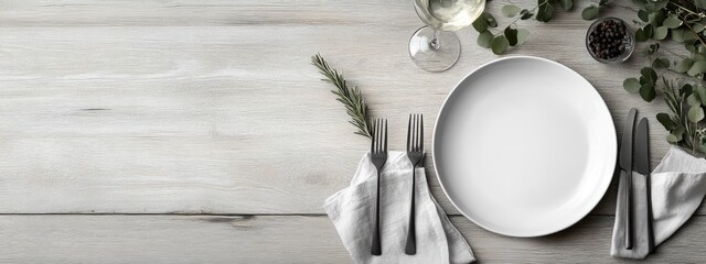Elegant white dinner plate set with cutlery on rustic wooden table surrounded by greenery and wine glass with space for text or menu.