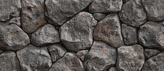 Obraz premium Textured stone wall background with irregularly shaped rocks in dark gray tones suitable for various design applications Copy Space