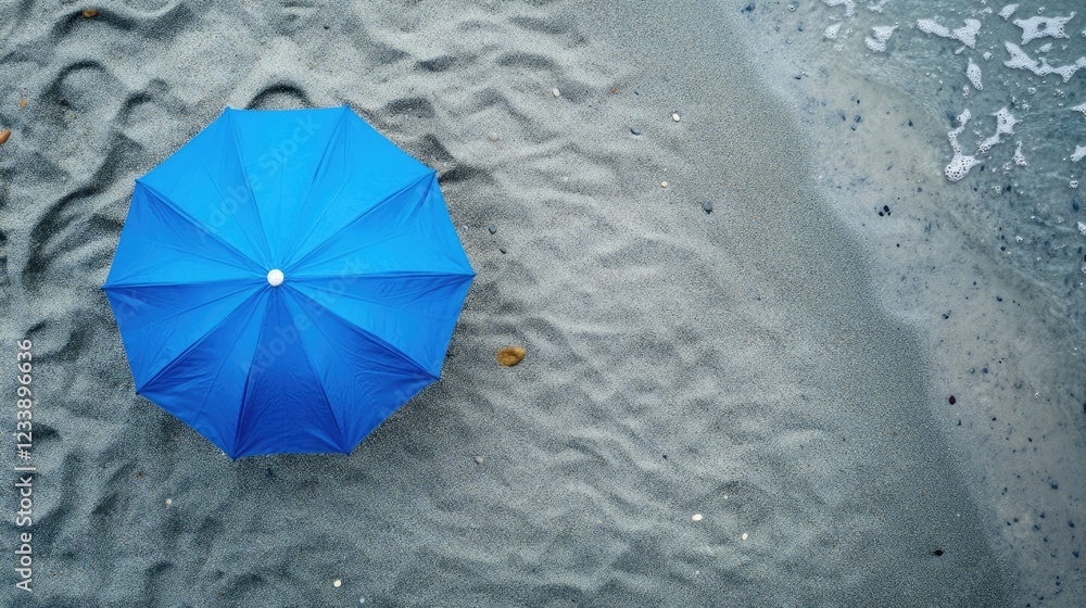 Poster aerial view of a blue beach umbrella resting on fine gray sand with gentle waves in the background a