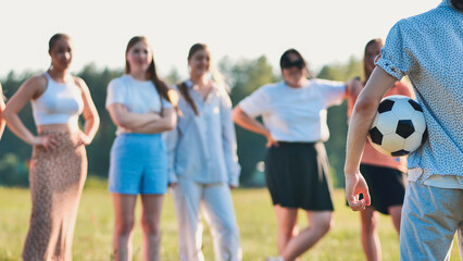 Obraz premium Young man with soccer ball approaching group of female friends in park, getting ready for a friendly game