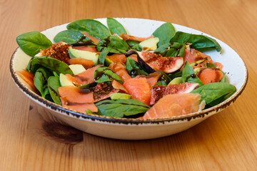 Healthy salad with smoked salmon, spinach, avocado and fig on wooden table
