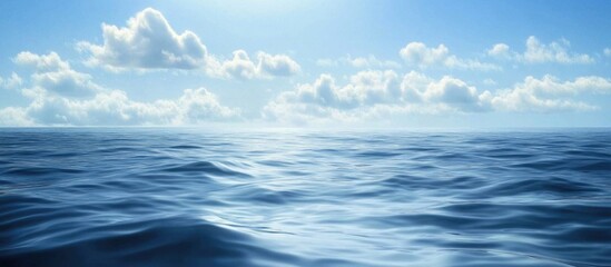 Fototapeta premium Vast ocean surface under a clear blue sky with soft clouds and sunlight reflection, ideal for backgrounds with Copy Space