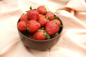 A bowl filled with fresh, ripe strawberries placed on soft, beige fabric with gentle folds.