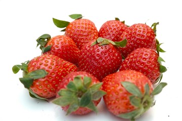 A close-up view of fresh, ripe strawberries with vibrant red color and green leafy tops, arranged neatly on a white background.