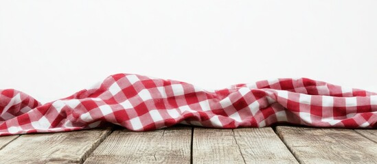 Fototapeta premium Red and white checkered tablecloth draped on wooden table with white background and ample copy space.