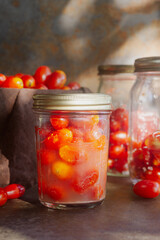 lacto fermented cherry tomatoes in a glass bottle jar on brown rustic table.