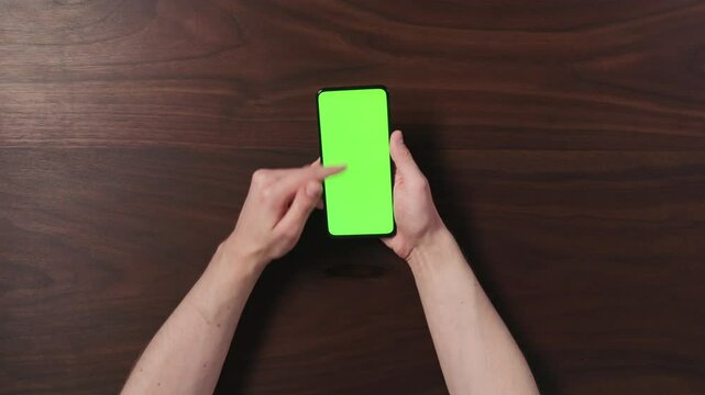 Top view man hand using smartphone with green screen over black walnut wood table