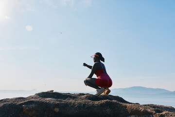 Woman in a red swimsuit squatting on a rock by the seaside under a clear blue sky