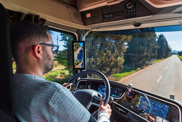 Truck driver seen from inside the cabin driving on a conventional two-lane road, one for each...