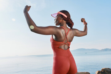 Confident woman in red activewear flexing her muscles by the seaside