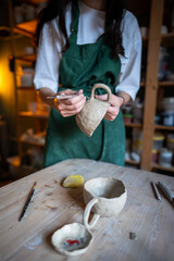 Female potter hands adjusting mug handle shape using clay carving knife, working meticulously in...