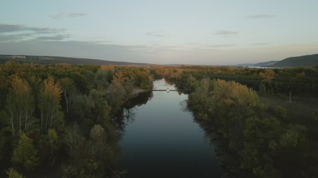 Autumn colors reflecting on calm river at sunset with footbridge appearing