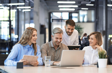 Four business professionals using laptop on desk discussing strategy company