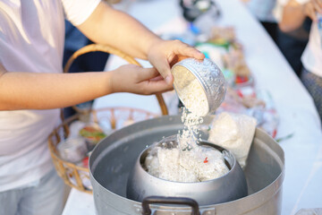 Thai person making a rice offering into an alms bowl during a traditional Buddhist merit-making ceremony in the morning.