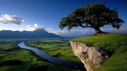 Serene Vista: A lone tree stands sentinel on a cliff overlooking a meandering river and picturesque mountain range, under a vibrant blue sky.