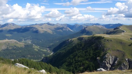Fototapeta premium Panoramic view of serene mountain ranges, lush green valleys, and winding roads under a blue sky with fluffy clouds.