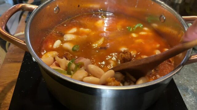 a close up view of the hand of a caucasian man&rsquo;s hand cooking a traditional spanish fabada at home