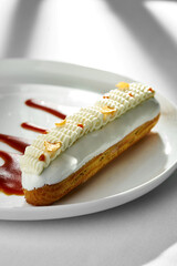 A classic eclair dessert, filled with creamy custard and topped with a drizzle of rich caramel sauce. The eclair is presented on a white plate