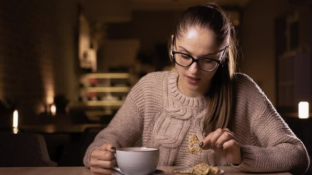 Relaxed woman in eyeglasses eating apples with nuts and drinking decaffeinated coffee in the night at cafe