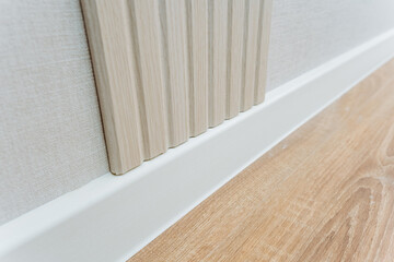 This image features a detailed closeup view of a wall that is adorned with a clean, white trim, alongside a beautifully polished wooden floor that adds character and warmth to the space