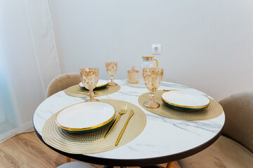 A beautifully arranged round dining table featuring elegant plates, shiny utensils, and stylish wine glasses placed on it for an inviting and enjoyable dining experience