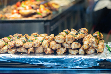 Close-up of juicy grilled chicken skewers paired with green peppers, displayed on a foil tray at a food stall.