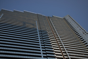 Low-angle view of a sleek modern skyscraper with reflective glass windows, set against a clear blue sky in an urban setting.