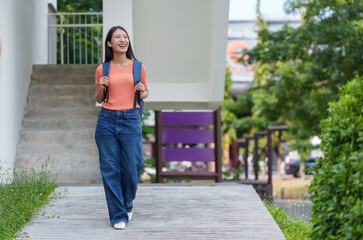 Cheerful university student is walking on campus with a backpack, enjoying the pleasant atmosphere and looking forward to a day of learning