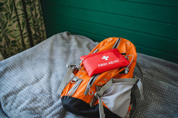Naklejka premium A vibrant bright orange backpack containing a wellstocked first aid kit, placed on a cozy bedspread, perfect for outdoor adventures and ensuring safety preparedness