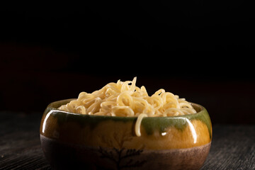 Steaming hot noodles being lifted from a  bowl by a pair of wooden chopsticks. The golden-yellow noodles cascade down, releasing wisps of steam that curl. Instant noodles on dark background. Food conc
