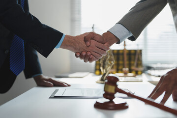 Two lawyers shaking hands after signing a contract in a law office, with a gavel and scales of...