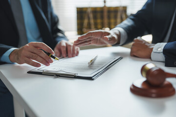Two lawyers are discussing a contract on a clipboard, with one lawyer pointing at a specific clause with a pen, while a gavel rests on the table, symbolizing legal proceedings and negotiations