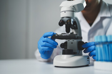 Scientist wearing blue gloves adjusting the stage of a microscope while conducting research in a laboratory environment, with test tubes nearby, symbolizing scientific investigation and analysis