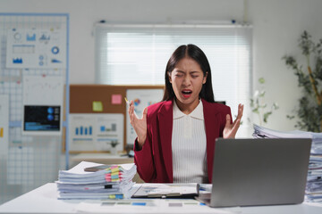 Young frustrated businesswoman is shouting at her laptop while sitting at her desk in the office, expressing her anger and frustration due to excessive workload and pressure