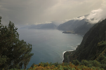 A breathtaking coastal landscape features rugged mountains shrouded in mist. The turbulent sea...