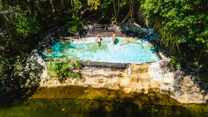 Two people enjoy a serene day in a secluded natural pool, embraced by the vibrant foliage of...