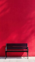 A black bench sits against a vibrant red wall, bathed in sunlight.