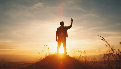 Fototapeta premium A silhouette raising one hand toward the sky at sunrise