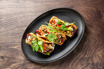 Delicious tacos served on a black plate, topped with fresh herbs, chopped vegetables, and vibrant spices. A colorful and appetizing dish perfect for food lovers.