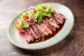 A beautifully arranged plate of sliced steak drizzled with sauce, garnished with fresh greens, cherry tomatoes, and onions. Perfect for food photography or culinary use.