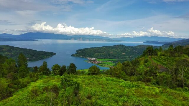 A 4K drone descends over the lush highlands of Lake Toba, capturing pine forests, rolling hills, and calm waters. The vast lake, with its central island, creates a stunning view